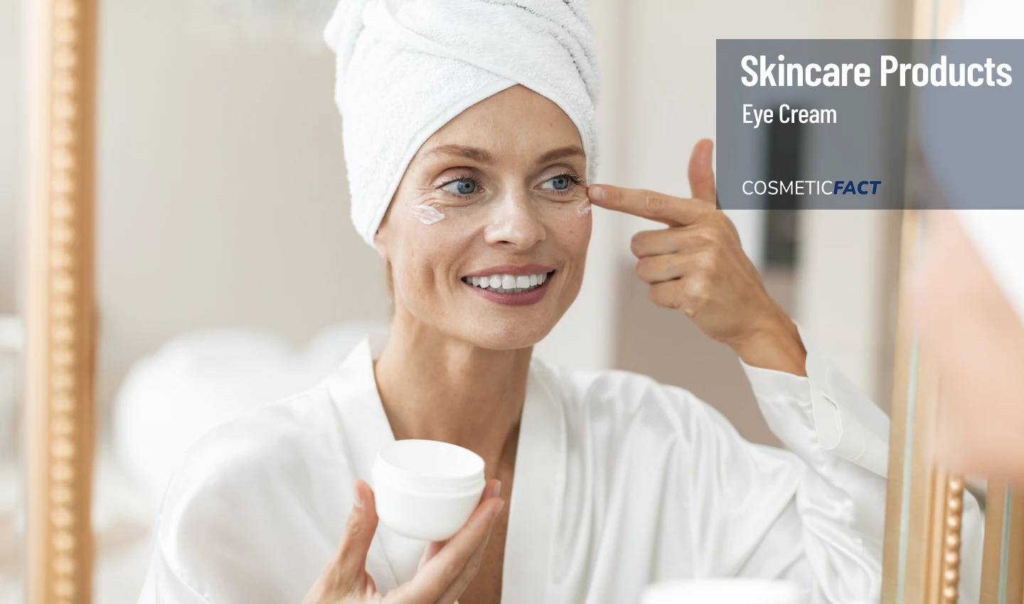 A mature woman smiles while applying eye cream to her under-eye area, enjoying the many benefits it provides for her skincare routine, including reducing fine lines, wrinkles, and dark circles.
