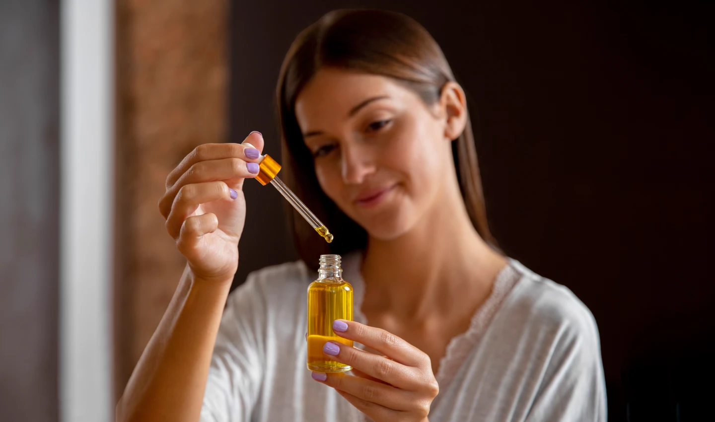 "Woman holding a bottle of face oil treatment for skincare routine, representing the information provided in Facial Oils 101