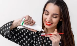 A young woman puts Best Toothpaste on her toothbrush in front of a bathroom mirror, representing the importance of choosing the best toothpaste for good oral health.