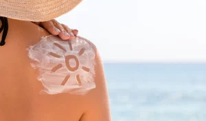 Woman applying sunscreen lotion to her arm on a sunny beach day.