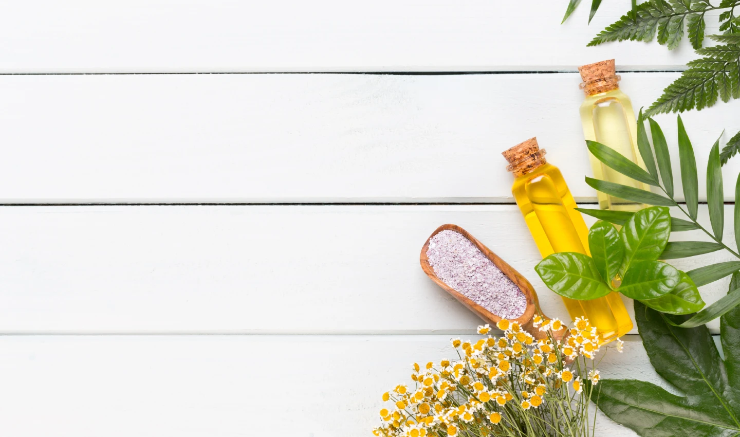 A photo of natural after-sun remedies including bottles of coconut oil, aloe vera gel, and lavender essential oil, alongside fresh flowers, all against a white background