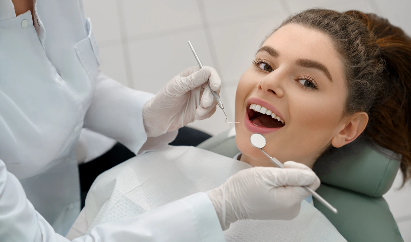 Patient receiving dental bonding benefits with a smile on her face while the dentist works on her teeth.