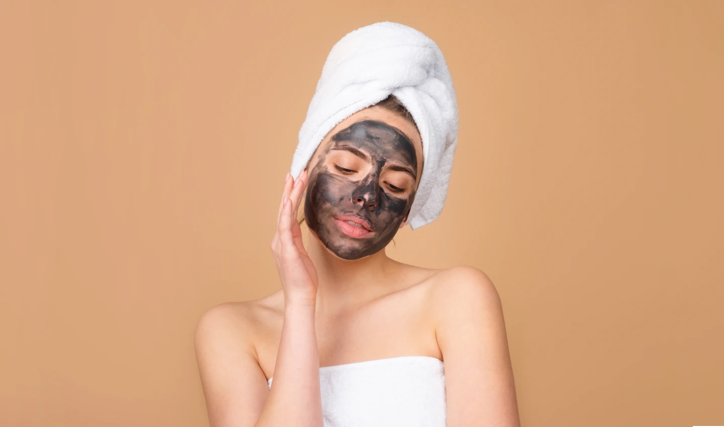 A young woman applies a charcoal mask to her face. Incorporating skincare masks benefits like this one into your beauty routine can help improve your skin's appearance and health.