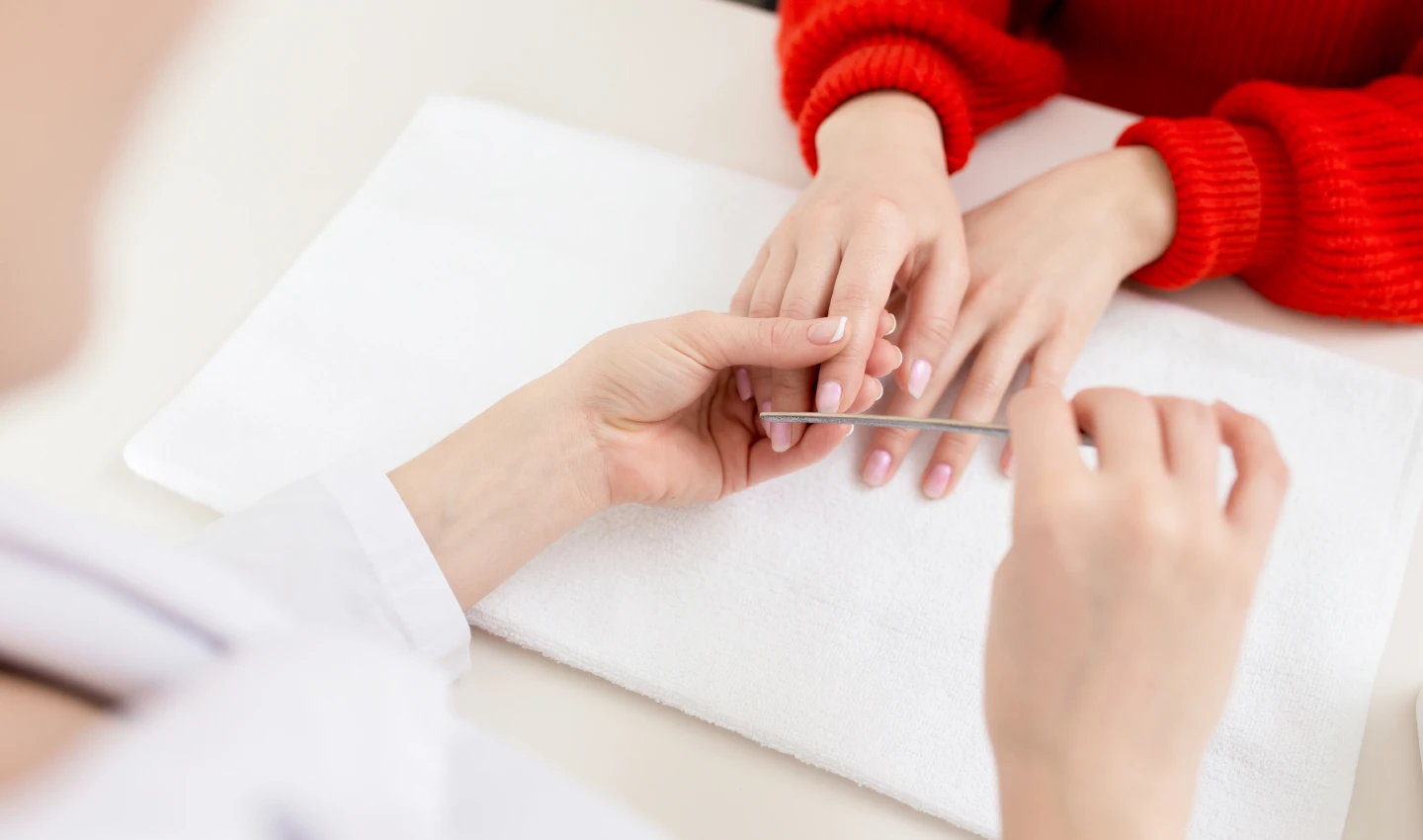A woman receiving a professional manicure as part of a professional nail treatment, with a skilled nail technician attending to her nails.