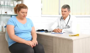 A woman looks unhappy as she discusses body beauty surgery financing with her doctor in a medical office setting.