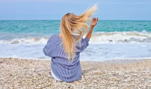 Woman with blonde hair blowing in the wind on the beach, showcasing the hairstyle "effortless beach waves".