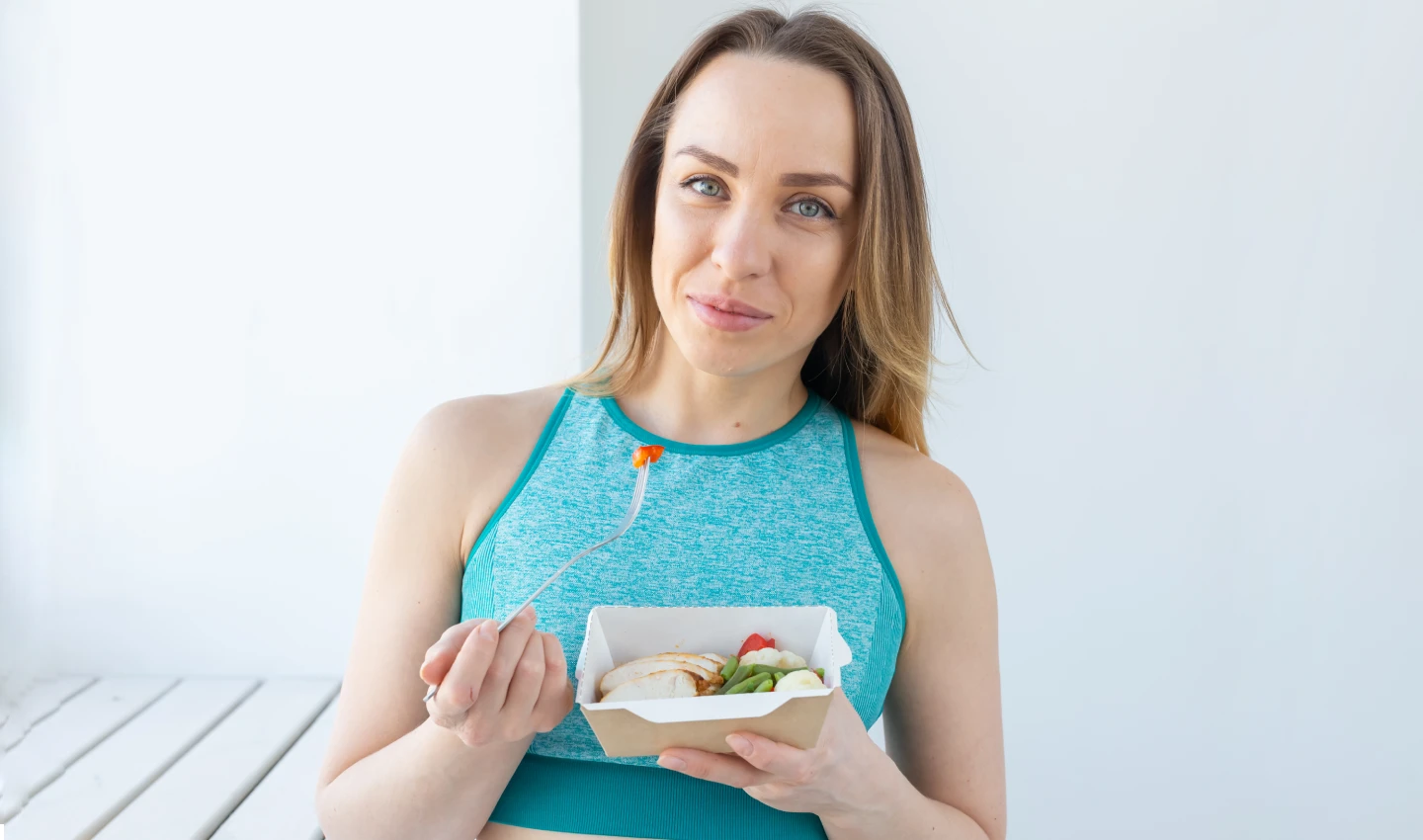 A woman smiles while eating healthy food, highlighting the importance of pre-operative diet for body surgery.