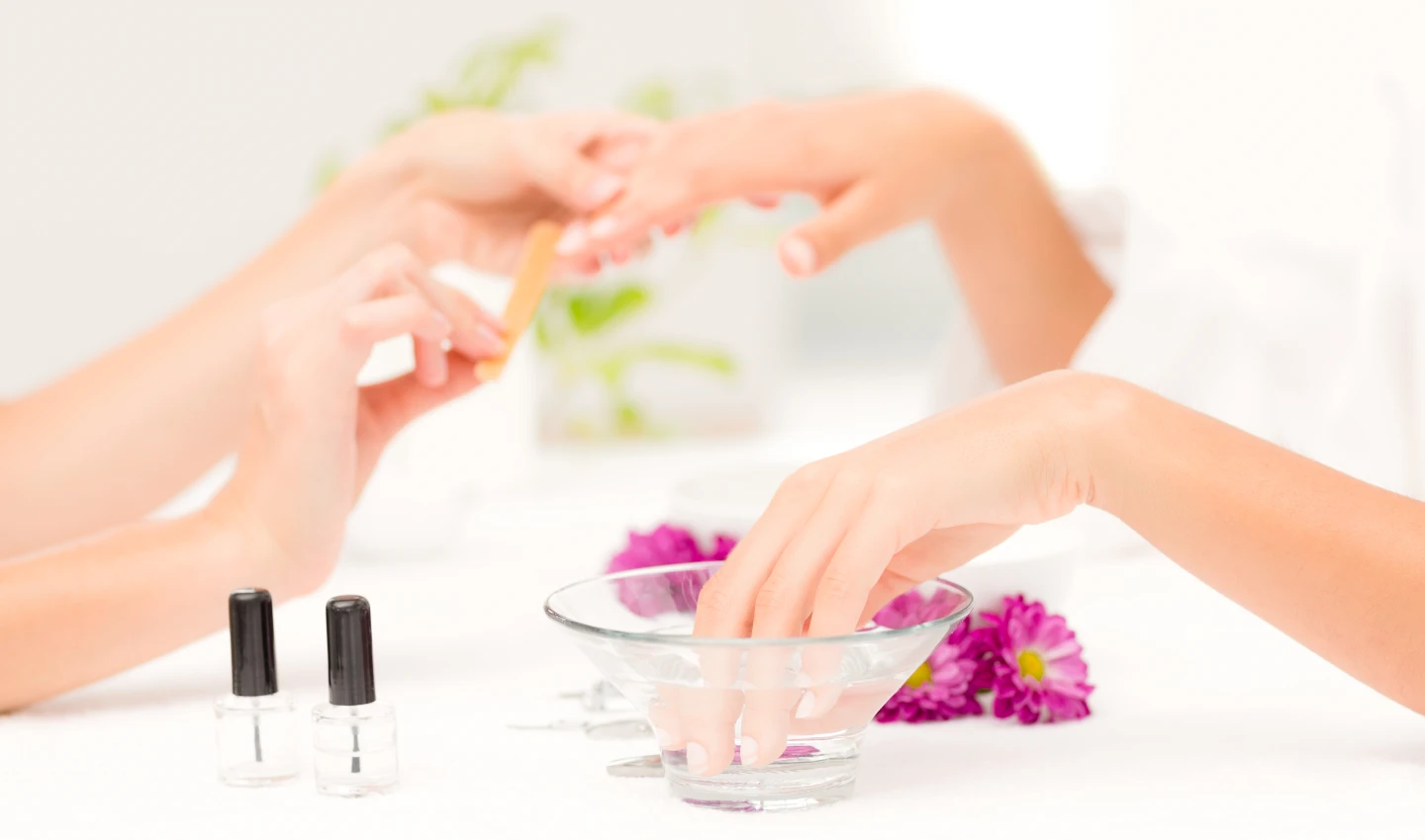 A woman's hand receives a natural nail treatment during a manicure session, surrounded by various natural nail products.