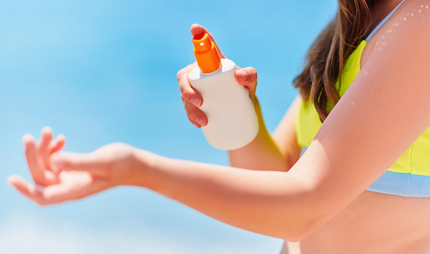 Woman applying sunscreen spray to her body for effortless sun protection.