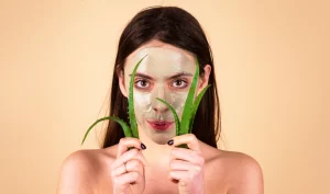 Girl holding a piece of aloe vera with a facial mask on her face, representing natural remedies for acne and clear skin.