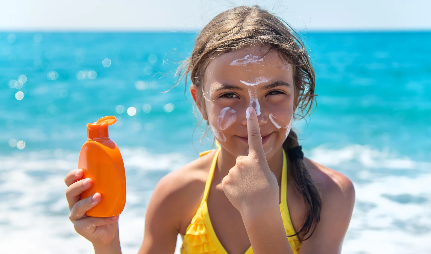 A child applying adventure-proof sunscreen to her nose, grinning happily.