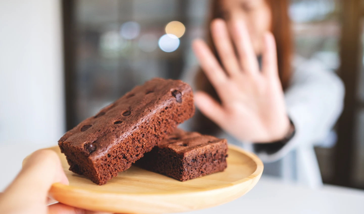 Woman saying no to chocolate cake as part of her teeth whitening diet to maintain a beautiful, bright smile after teeth beauty surgery.