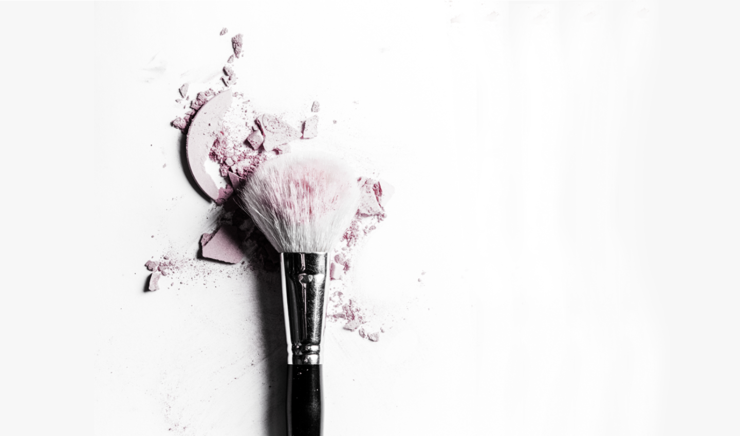 A makeup brush with synthetic bristles is shown alongside a pot of violet blush. The brush's design allows for precise application and represents the evolution of makeup brush technology.