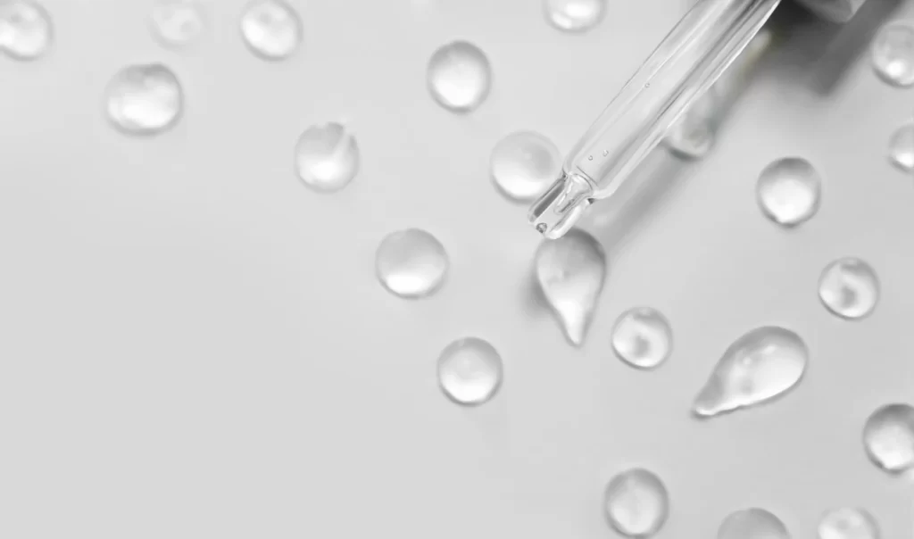 Hyaluronic Acid Serum dropper bottle with drops on white background, a skincare product for deep hydration and plumping effects.