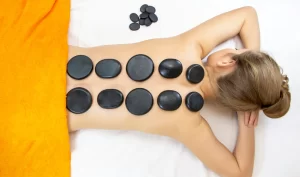 Person receiving hot stone therapy with stones placed on her back for relaxation and rejuvenation.