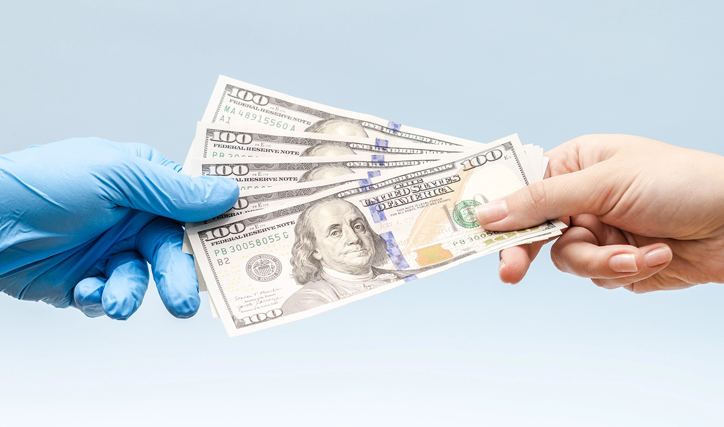 Hand of a person giving money to a surgeon with gloves, representing if the facelift surgery worth the cost.