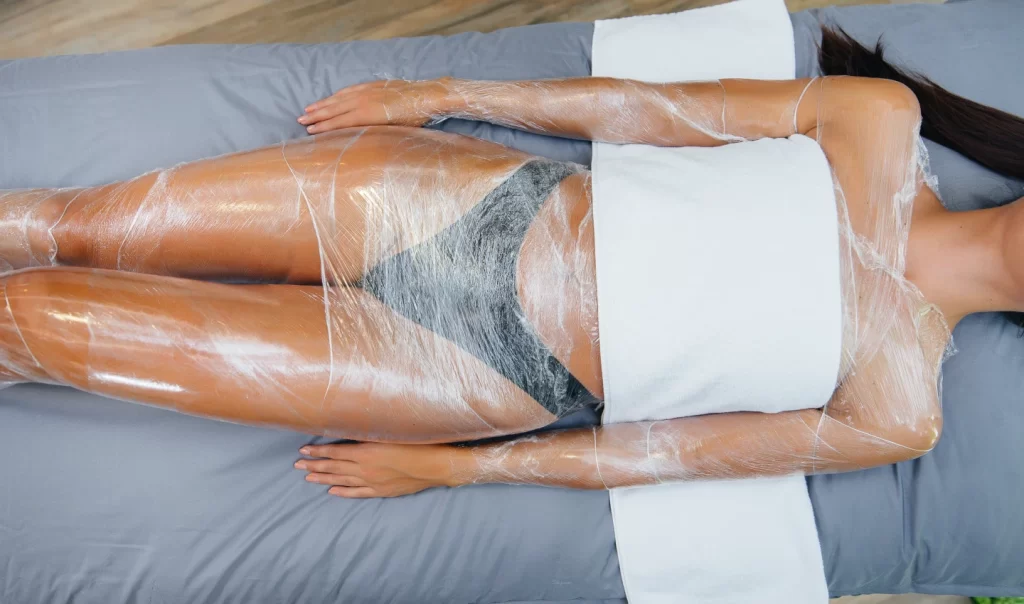 Woman enjoying hot stone therapy session with phone nearby for body wraps benefits.