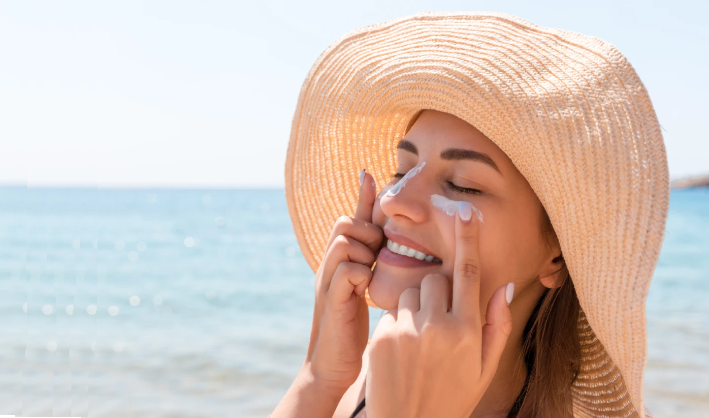 Woman putting sunscreen cream on her face at the beach. Highlighting the importance of Sun Protection Skincare for healthy skin.