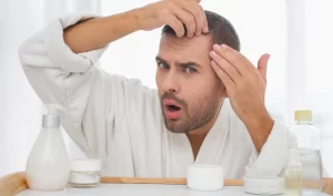 A man in front of the mirror looking panicked due to hair loss, highlighting the need for effective hair loss prevention treatments like scalp massage and natural hair products.
