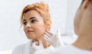 Image of a female dermatologist examining another woman's neck and jawline with her fingers. The image represents the process of receiving Kybella treatment from a qualified dermatologist to achieve a defined jawline.