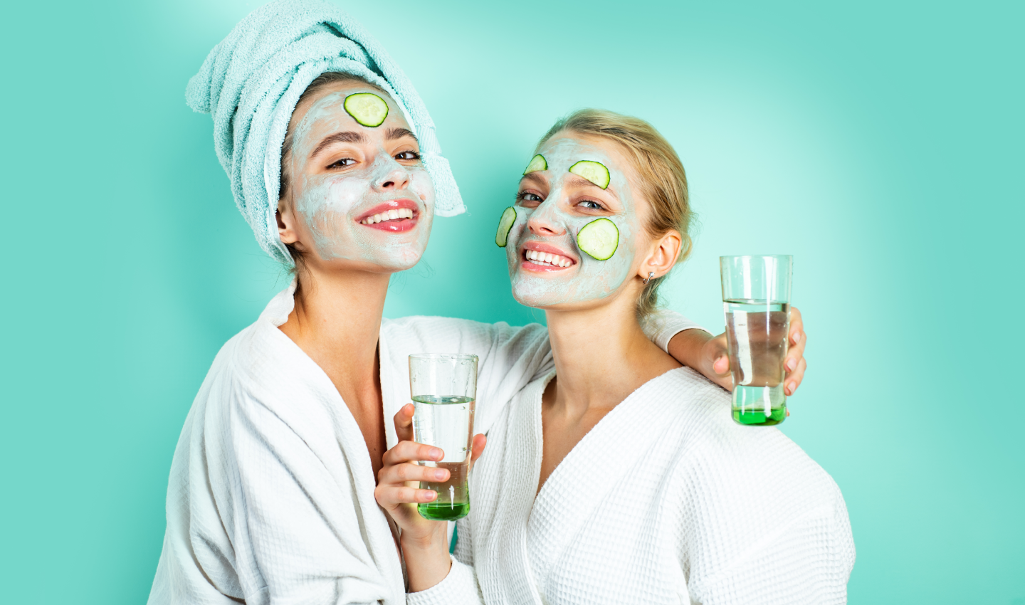 Two women smiling with facial masks on and holding glasses of water, representing Hydra Facial for hydration