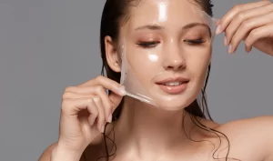 A young woman smiles as she peels off a hydrating facial mask from her face, revealing glowing, hydrated skin. The image highlights the benefits of hydrating masks for revitalizing dry and dehydrated skin.