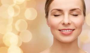 An image of a young woman with even, glowing skin smiling at the camera. The image emphasizes the importance of achieving a luminous glow for a glowing complexion and the benefits of brightening treatments.