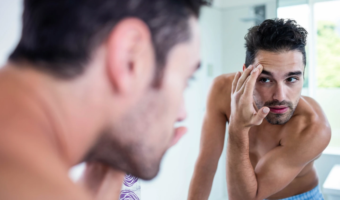 Shaved man looking at mirror with a satisfied expression on his face, representing skincare mistakes for men article.