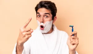 A man with shaving foam on his face, preparing to groom his facial hair according to expert tips for men's facial hair grooming.