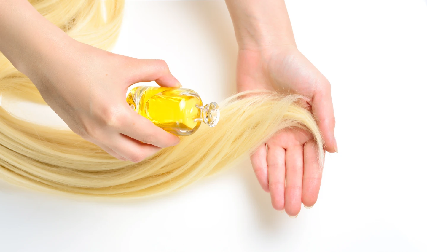 A person applying essential hair treatment to a bunch of hair in their hand.