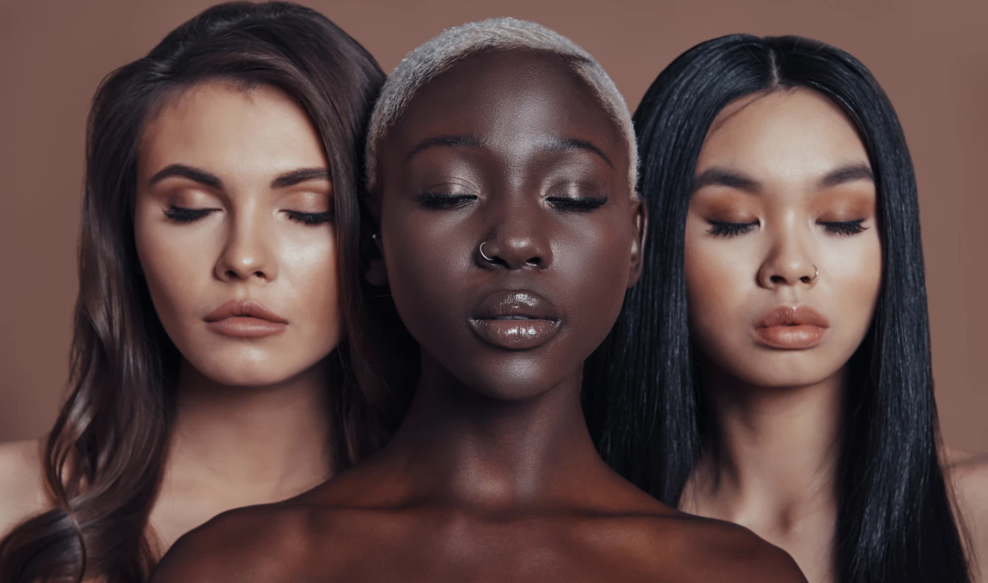 Three women of different skin tones representing various ethnicities and nationalities, standing in front of the camera with eyes closed, embracing diversity and inclusivity in beauty with global face shades designed to match every skin tone and complexion.