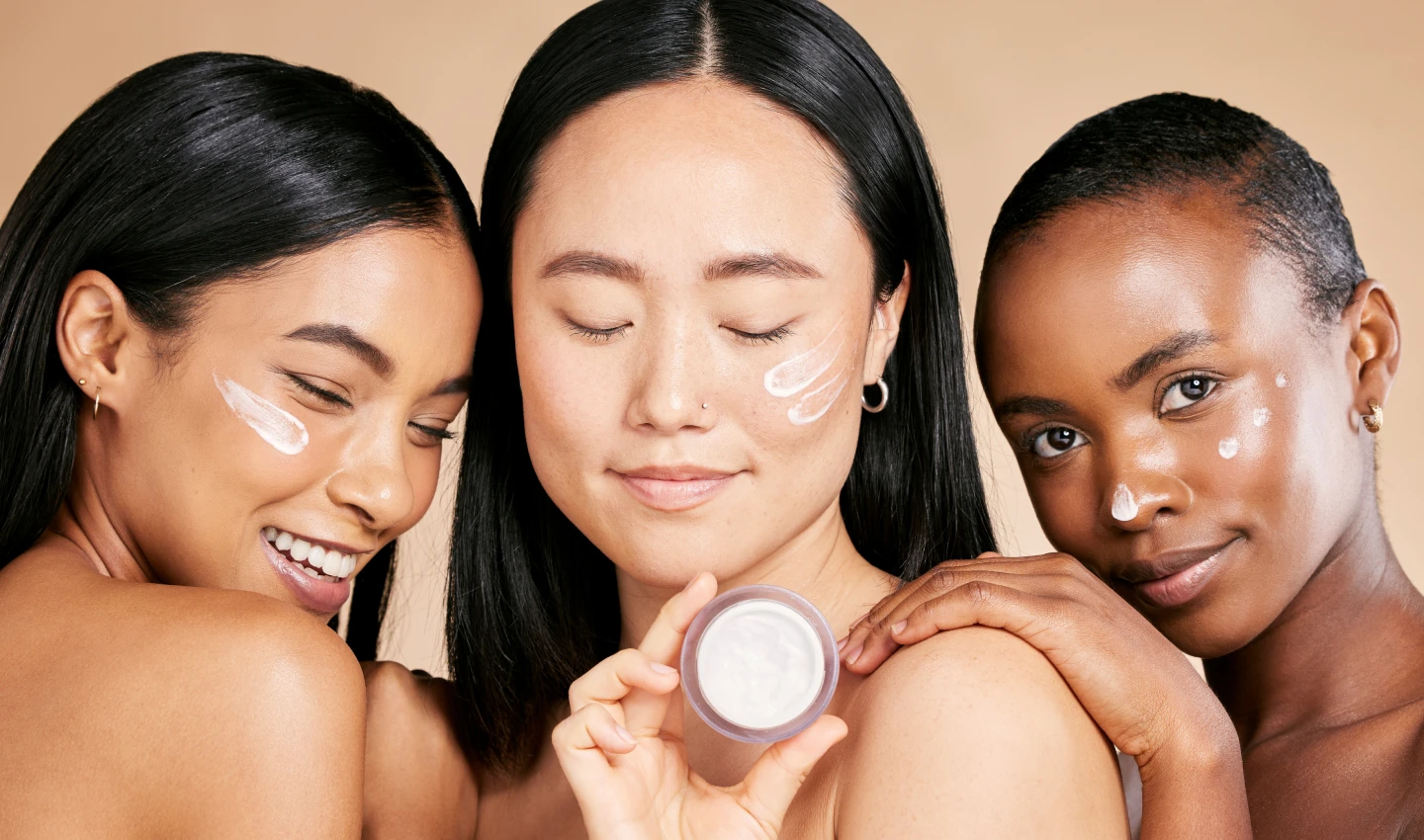 Three women of different skin colors and ethnicities holding up and trying on different foundation shades to find their perfect match