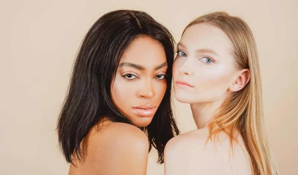 Two young women, one with bronzed skin and one with fair skin, looking at the camera seductively.