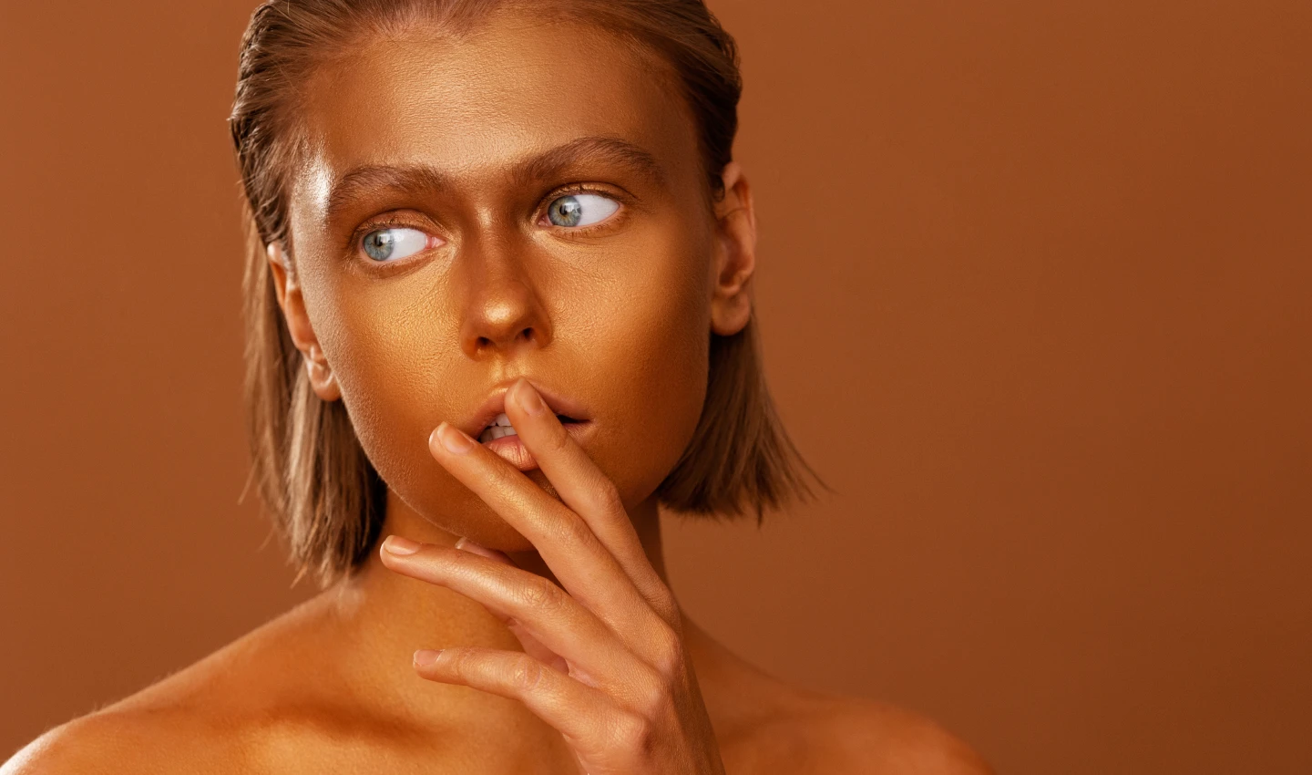 Woman with a tan face holding a bottle of fake tan, representing the skincare benefits of using fake tan.