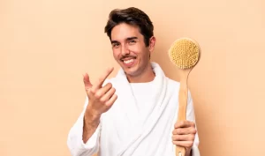 A man uses a dry brush on his skin while holding a men's dry brushing set.