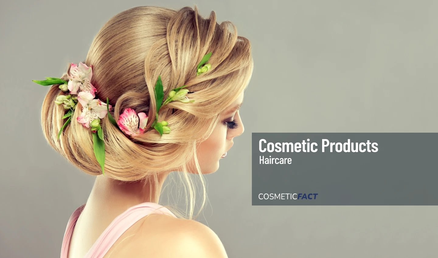 Young and beautiful woman with blonde hair styled in an elegant updo with natural pink blossoms and flowers inserted into the hairdo.