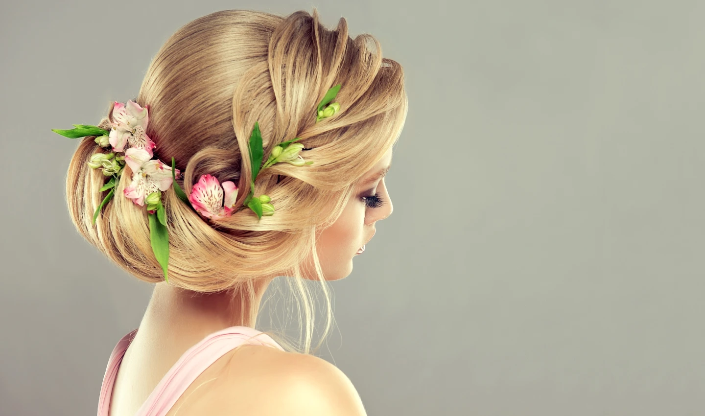 Young and beautiful woman with blonde hair styled in an elegant updo with natural pink blossoms and flowers inserted into the hairdo.