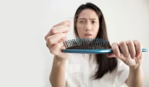 An anxious woman taking out loose strands of hair from a hairbrush, emphasizing the importance of restorative hair treatments for repairing and strengthening damaged hair.