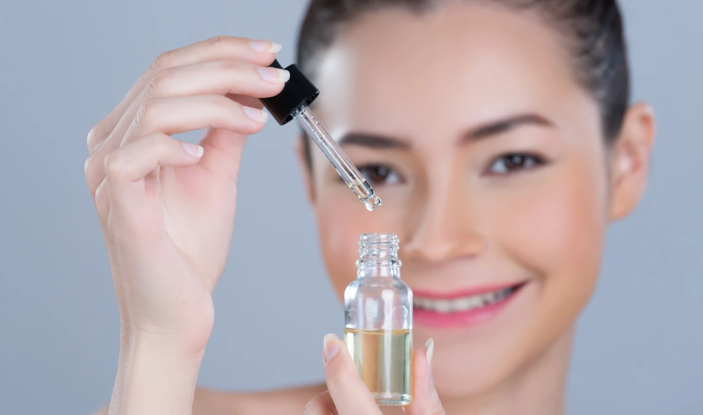 Woman holding and smiling at a bottle of facial oil for sensitive skin.