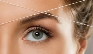 A close-up image of a woman having her eyebrows shaped using precision techniques with tweezers and a brow brush, with brow powder or pencil being used to fill in any gaps.
