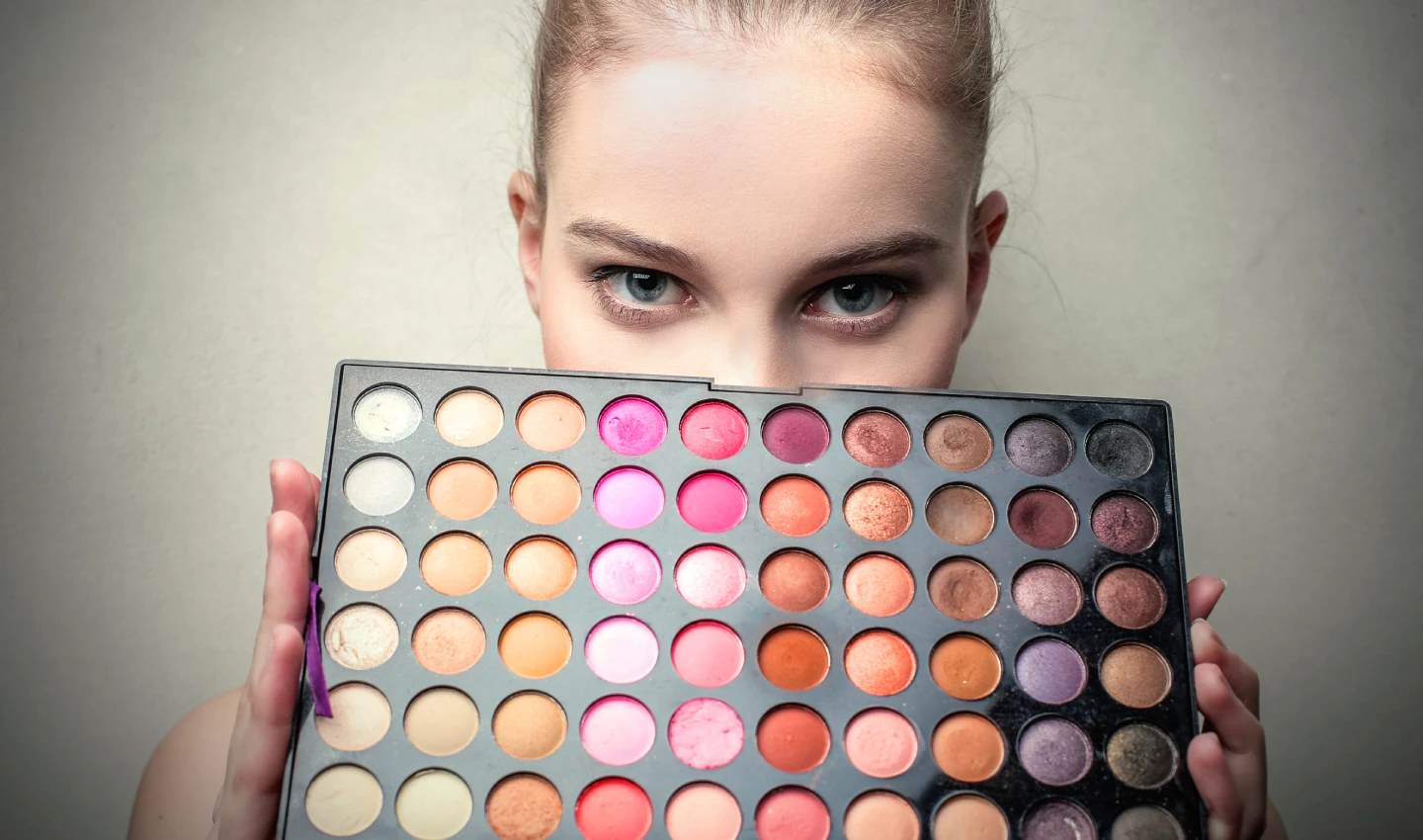 A young lady holding a large palette of versatile eye shadows with a wide range of colors, perfect for creating stunning and versatile makeup looks suitable for any occasion.