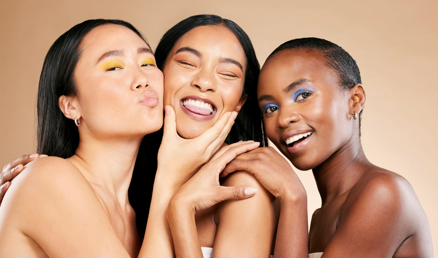 Three women of different ethnicities with expressive and artistic makeup looks using global face shades, designed to match a wide range of skin tones from around the world, smiling at the camera