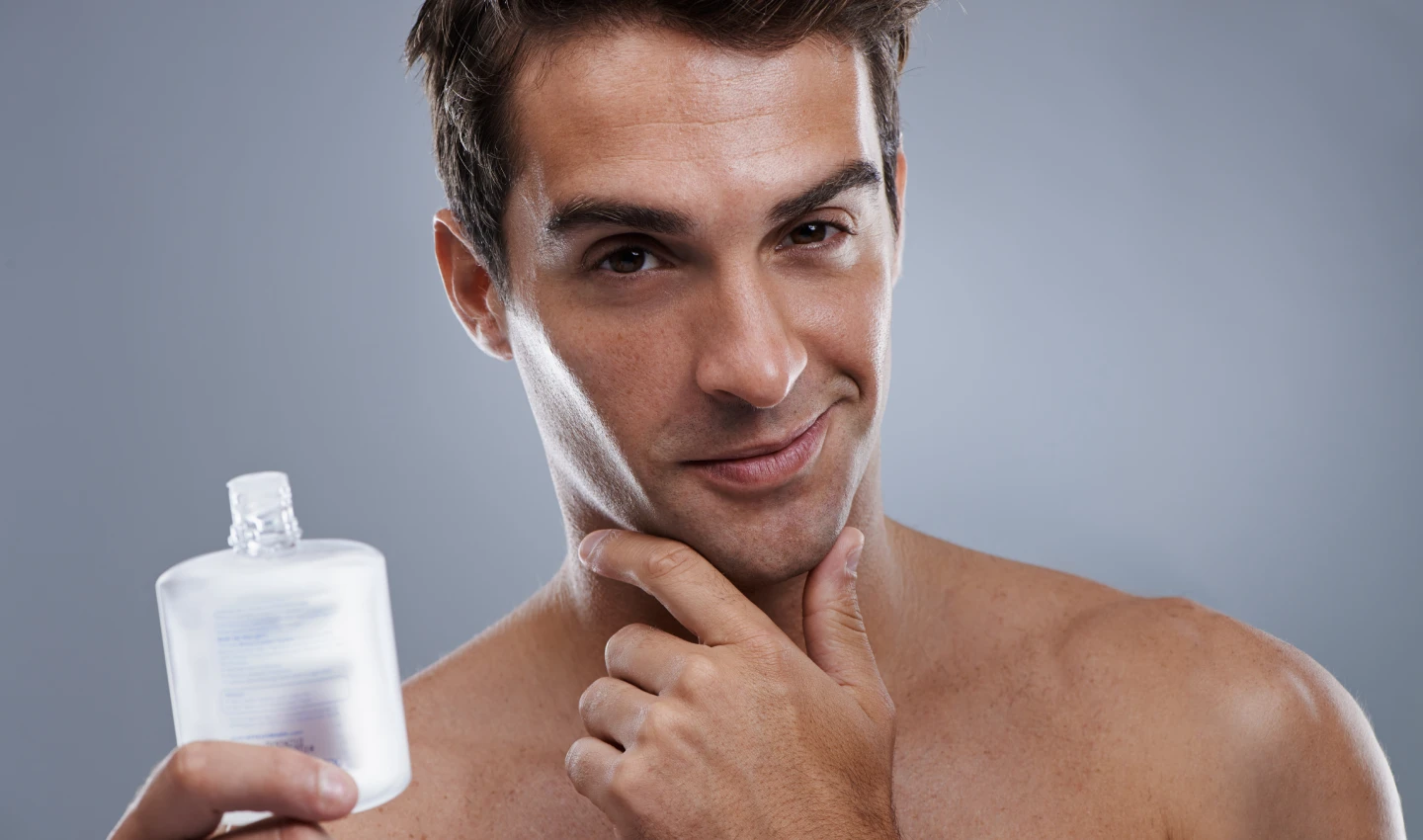 A man with a shaved face smiles after using aftershave, emphasizing the benefits of including aftershave in a men's skincare routine.