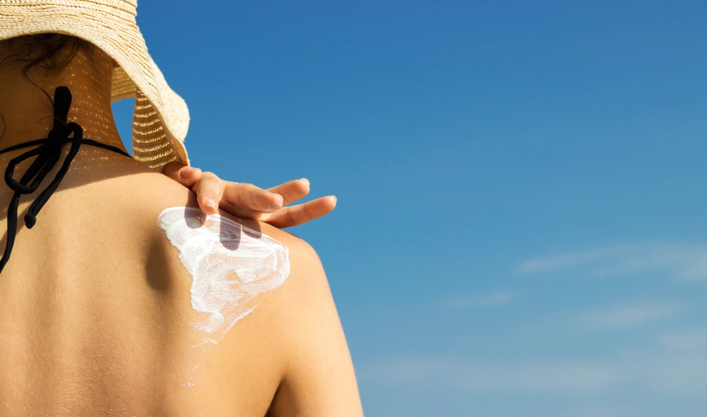 Woman applying moisturiser with SPF to her shoulders at the beach.