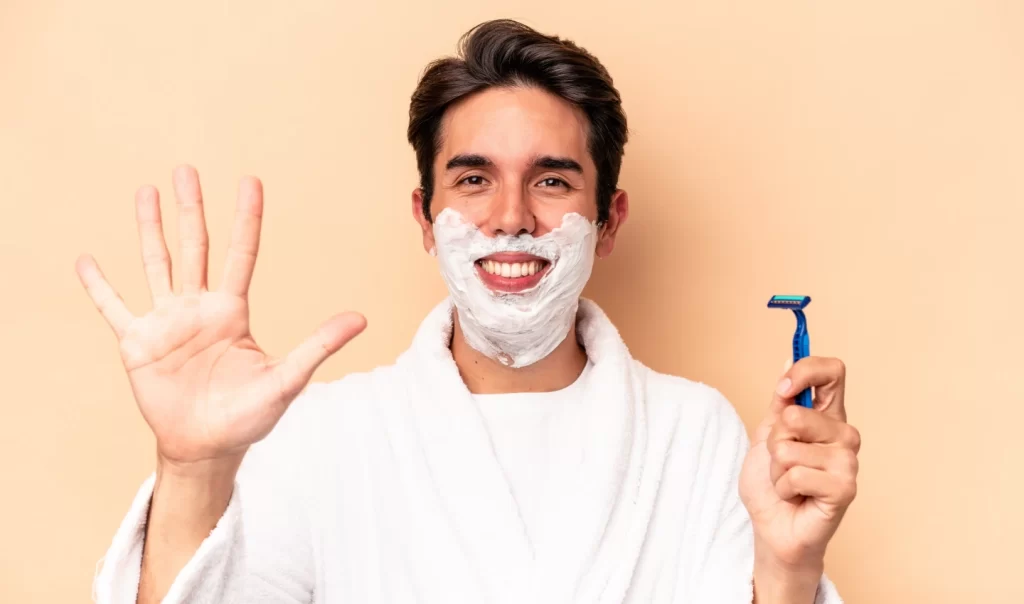 A smiling man with shaving foam on his face, promoting natural aftershave alternatives for men and featuring witch hazel extract.