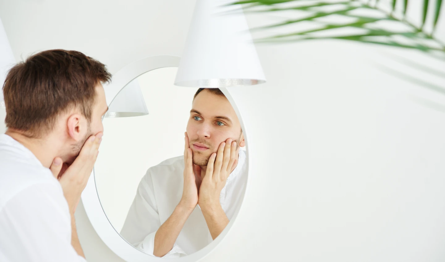 A man looking at himself in the mirror after using one of the best facial cleansers for men's skin types. He has a cleanly shaven face and looks happy and refreshed.