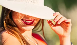 Woman with beautiful lipstick and hat holding a tube of sun-protective lip balm for outdoor adventures.