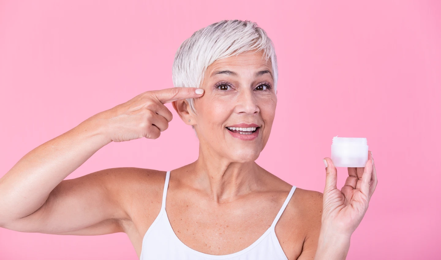 Middle-aged woman holding a jar of anti-aging moisturiser, looking happy and radiant.
