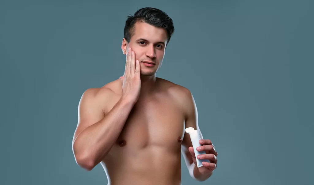 Men's Body Care for Sensitive Skin - An image of a well-shaped young man looking at the camera and touching his face. The man's healthy and glowing skin emphasizes the importance of taking care of your skin, especially if you have sensitive skin.