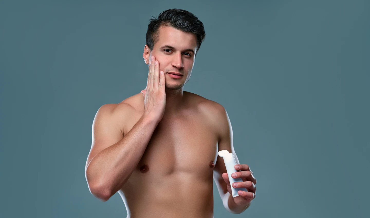 Men's Body Care for Sensitive Skin - An image of a well-shaped young man looking at the camera and touching his face. The man's healthy and glowing skin emphasizes the importance of taking care of your skin, especially if you have sensitive skin.